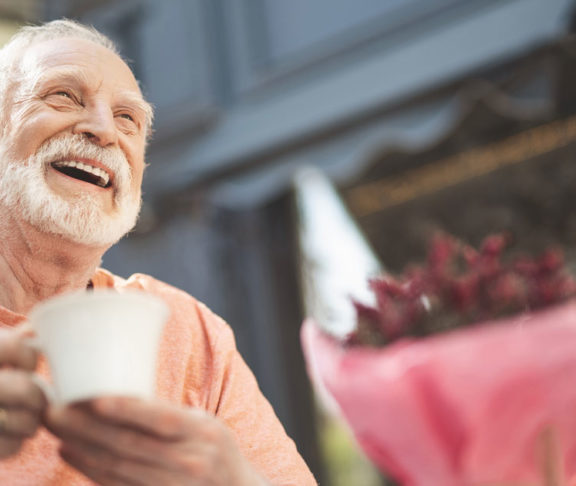 Laughing elderly man drinking tea outdoors