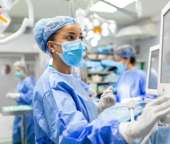Anesthetist Working In Operating Theatre Wearing Protecive Gear checking monitors while sedating patient before surgical procedure in hospital