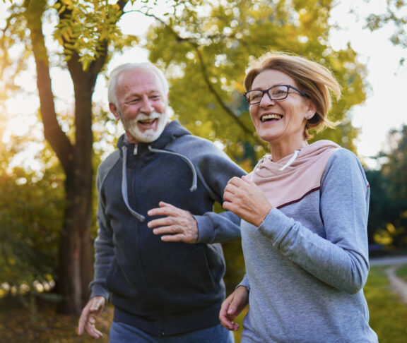 Cheerful active senior couple jogging in the park