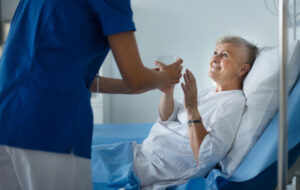 Young nurse giving glass of water to senior patient at a hospital ward.