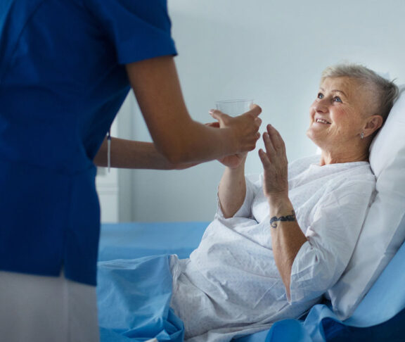 Young nurse giving glass of water to senior patient at a hospital ward.