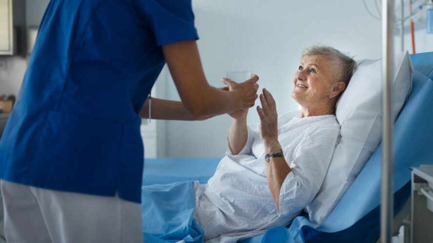 Young nurse giving glass of water to senior patient at a hospital ward.