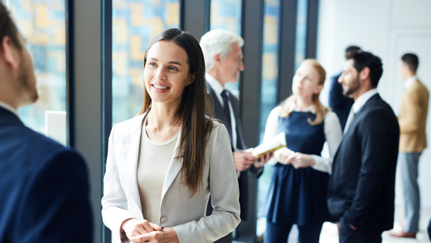 Smiling pretty young business lady in jacket talking to colleague and discussing business forum topics during break