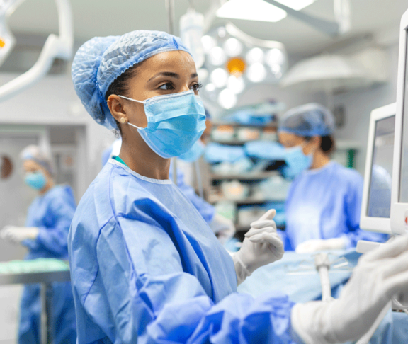 Anesthetist Working In Operating Theatre Wearing Protecive Gear checking monitors while sedating patient before surgical procedure in hospital
